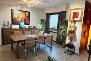 Un espace de salle à manger moderne, avec une table et des chaises en bois, une statue de Bouddha et un tableau accroché au mur.