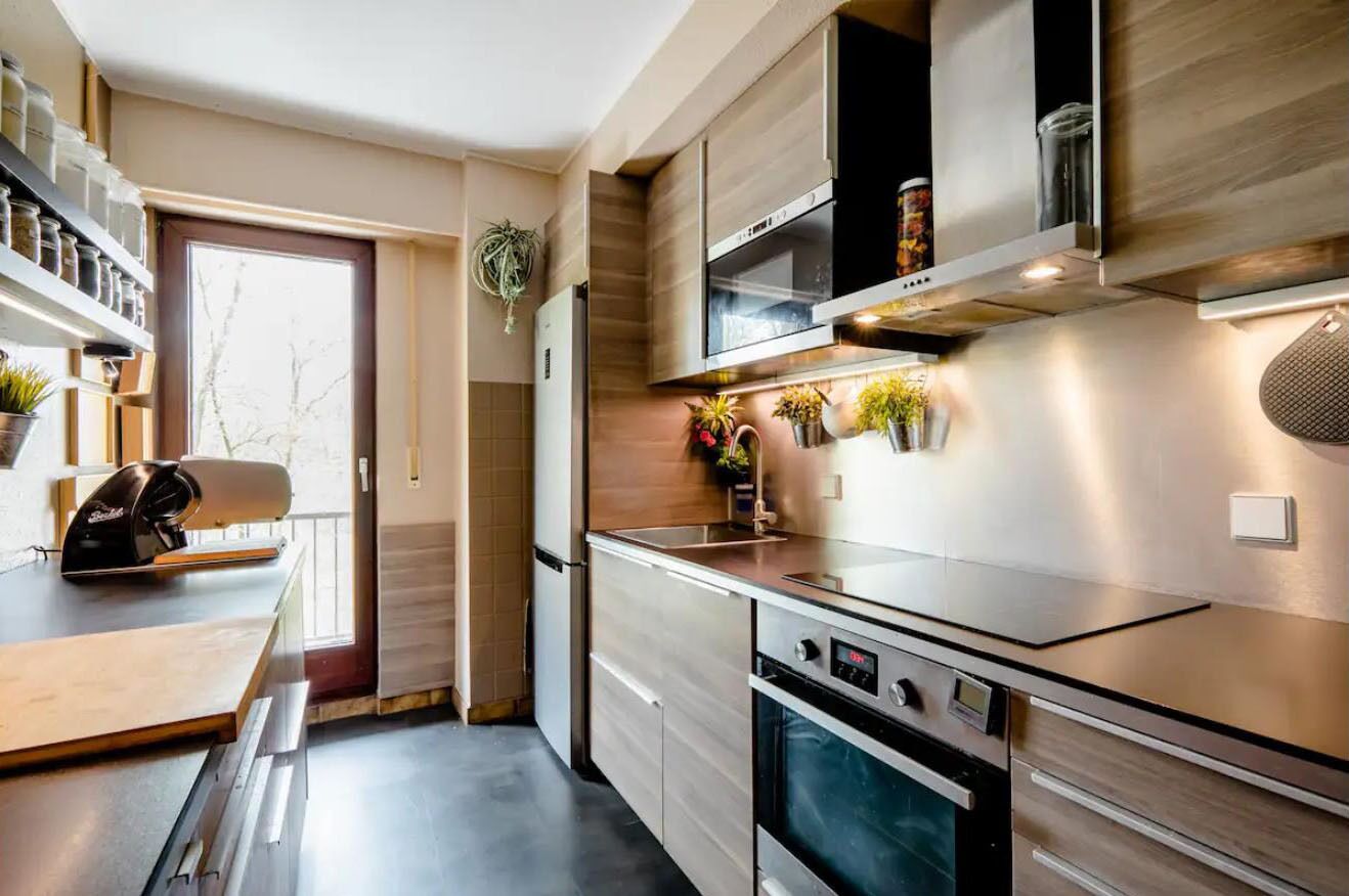 Une cuisine moderne dotée d’appareils électroménagers intégrés, de meubles de rangement en bois et d’une fenêtre laissant entrer la lumière naturelle.