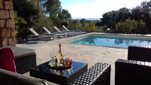 A poolside area with lounge chairs, a table with a bottle and glasses, and a view of the pool and surrounding trees. - Peaceful villa with quality services at the gates of Haut-Var - Flayosc (Flayosc)
