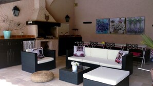 Un espace extérieur accueillant, aménagé avec des meubles en osier et un canapé blanc, une petite table ronde et une plante en pot.