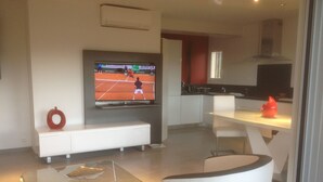 A modern kitchen with a flat-screen TV, a glass coffee table, and a dining area with a white chair. - Charming apartment in property with pool and large park (Saint-Raphaël)