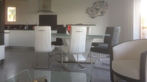 A modern kitchen with white cabinets, a glass dining table, and two chairs. - Charming apartment in property with pool and large park (Saint-Raphaël)