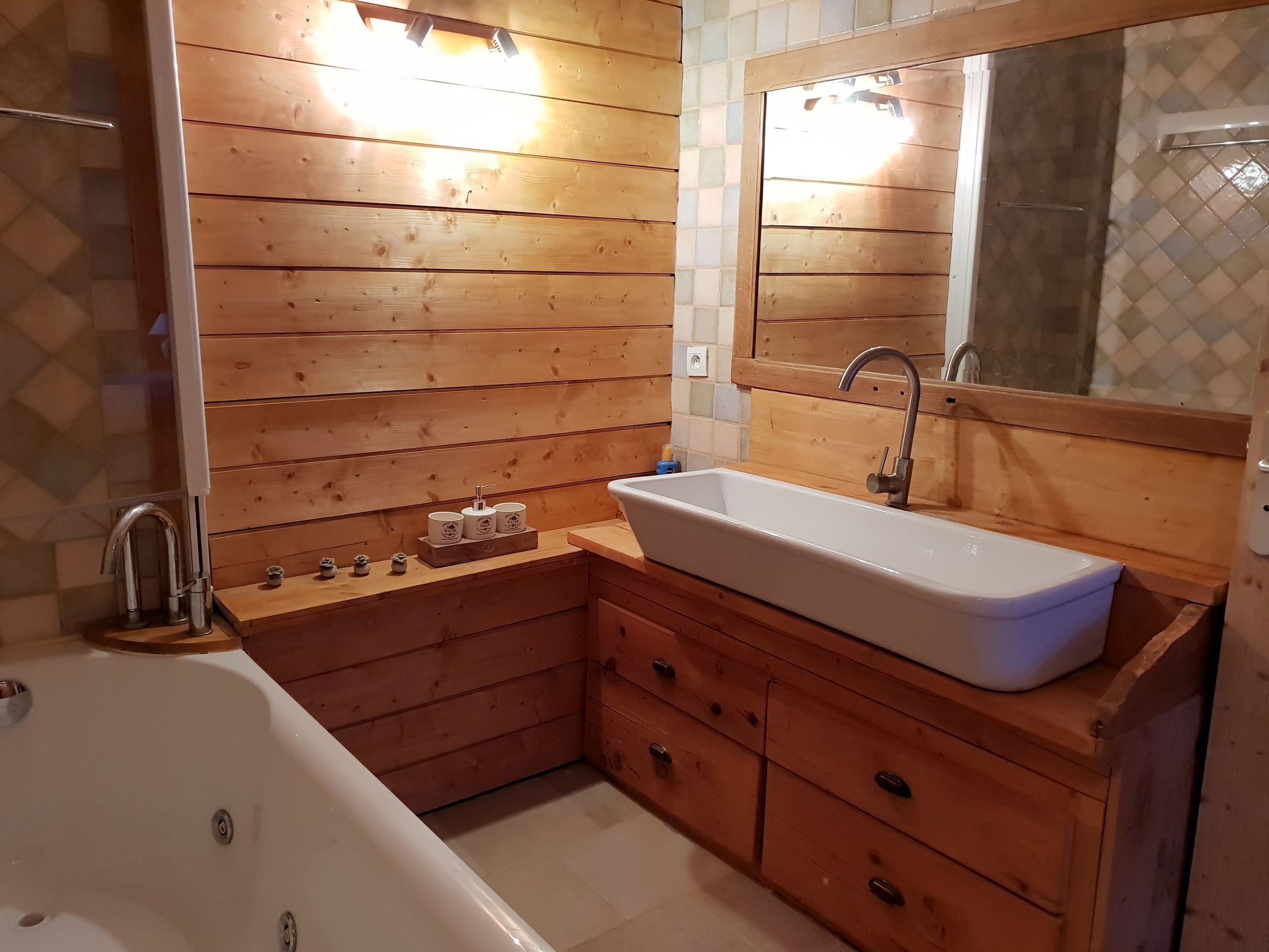 Un baño de madera con lavamanos blanco, un espejo y una bañera.