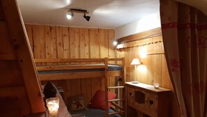 Een gezellig vakantiehuisje met houten wanden en een stapelbed. Er staat een klein tafeltje met een kaars en een decoratief object.