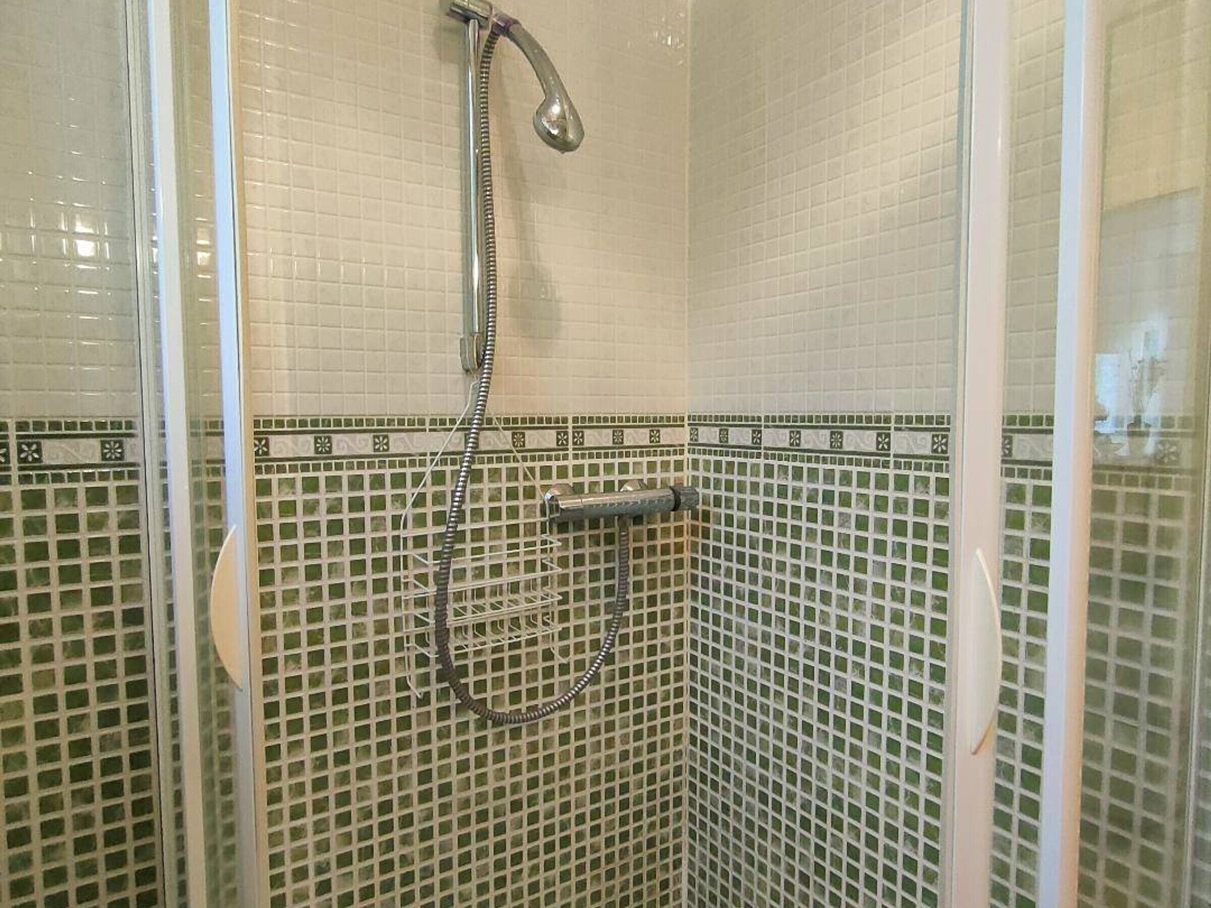 A shower with a handheld showerhead and a wall-mounted faucet, surrounded by mosaic tiles.