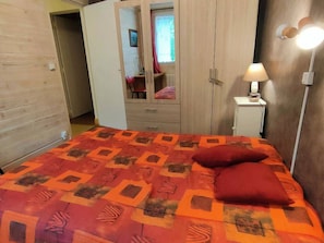 Um quarto com cama, guarda-roupa, mesa de cabeceira e abajur.