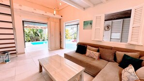 Ein modernes Wohnzimmer mit einem beigefarbenen Sofa, einem Glastisch und Blick auf einen Swimmingpool durch eine Schiebetür.