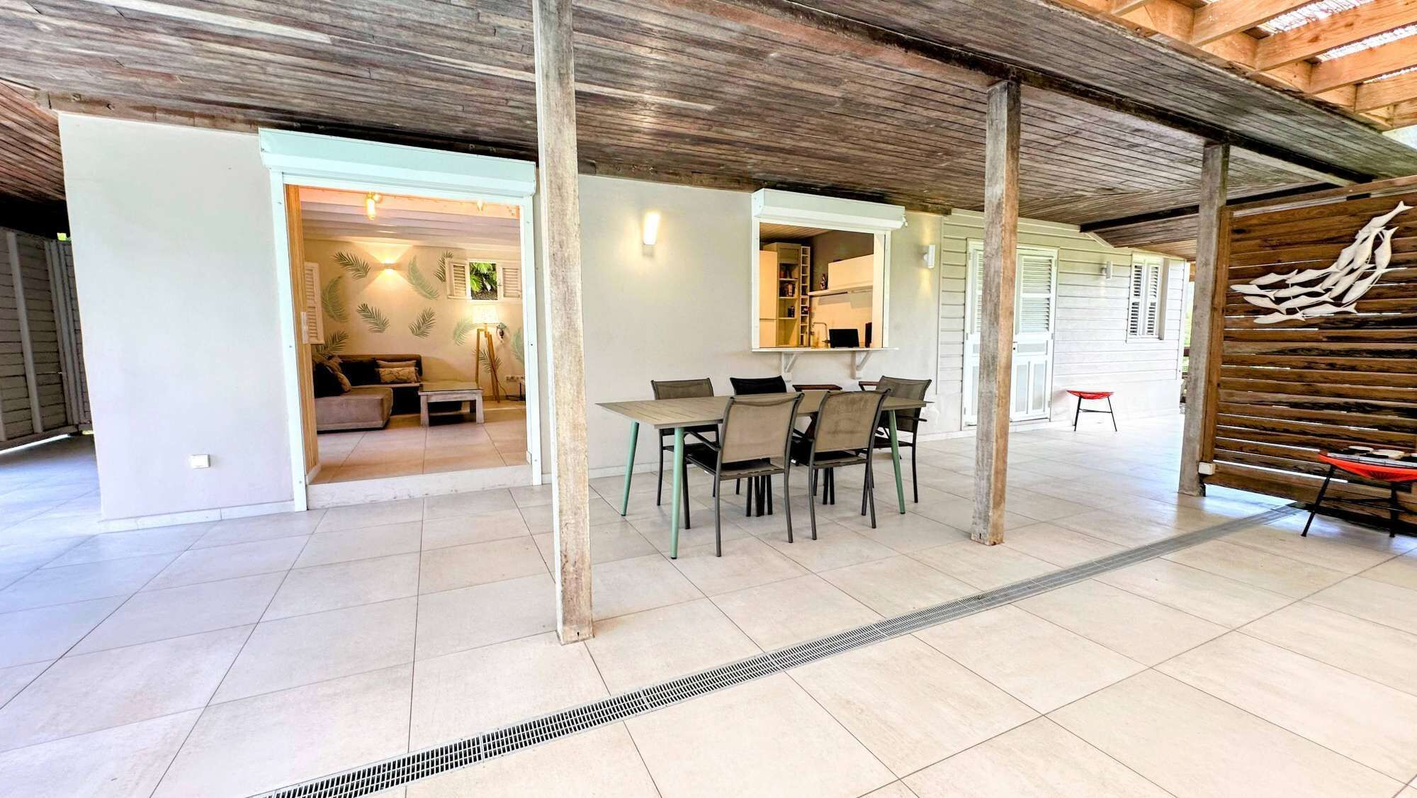A spacious dining area with a high ceiling and exposed beams, a kitchen visible through an open doorway, and a dining table with chairs.