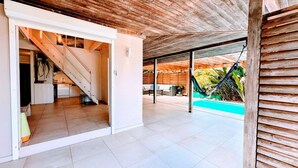 Ein modernes Interieur mit einer Treppe, die zu einer Küche führt, einem Poolbereich inklusive Hängematte und einer Holzbalkendecke.
