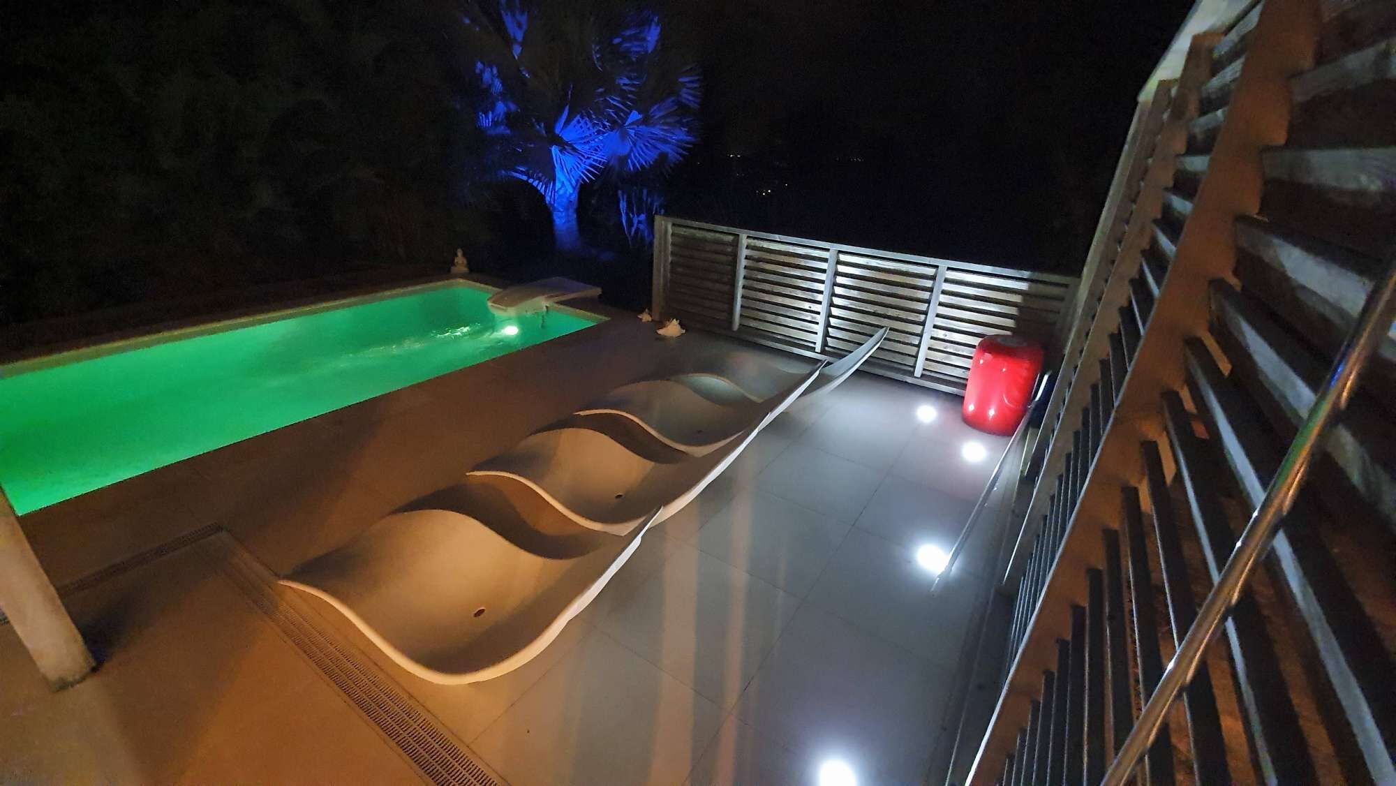 Una piscina con diseño de borde ondulado, una fuente de agua roja y una barandilla de metal.