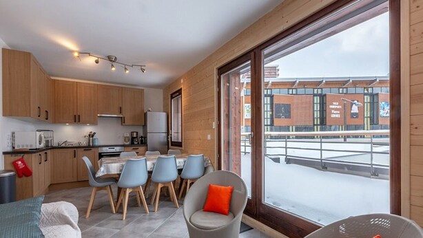 A modern kitchen with wooden cabinets, a dining area with chairs, and a large window offering a view of a building with advertisements. - Charming apartment in La Plagne with equipped kitchen and quick access to the slopes (La Plagne)