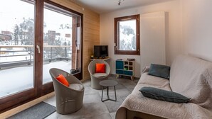 A modern living room with a sofa, two armchairs, a small table, and a TV. There is a large window with a view of a snowy landscape. - Charming apartment in La Plagne with equipped kitchen and quick access to the slopes (La Plagne)