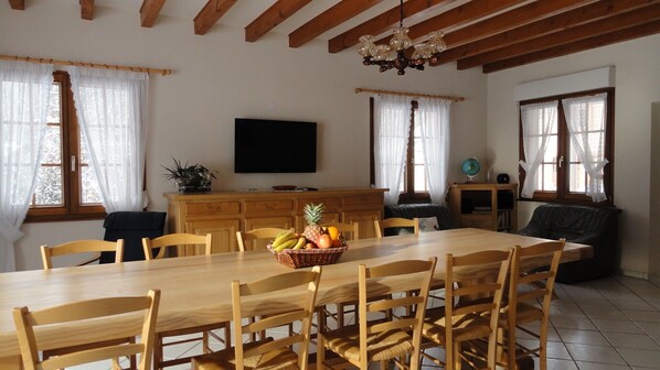 Un comedor con una mesa y sillas de madera, una cesta de frutas y un televisor en la pared.
