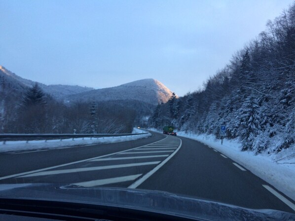 Una carretera nevada en la montaña con baranda de seguridad y un vehículo a lo lejos.