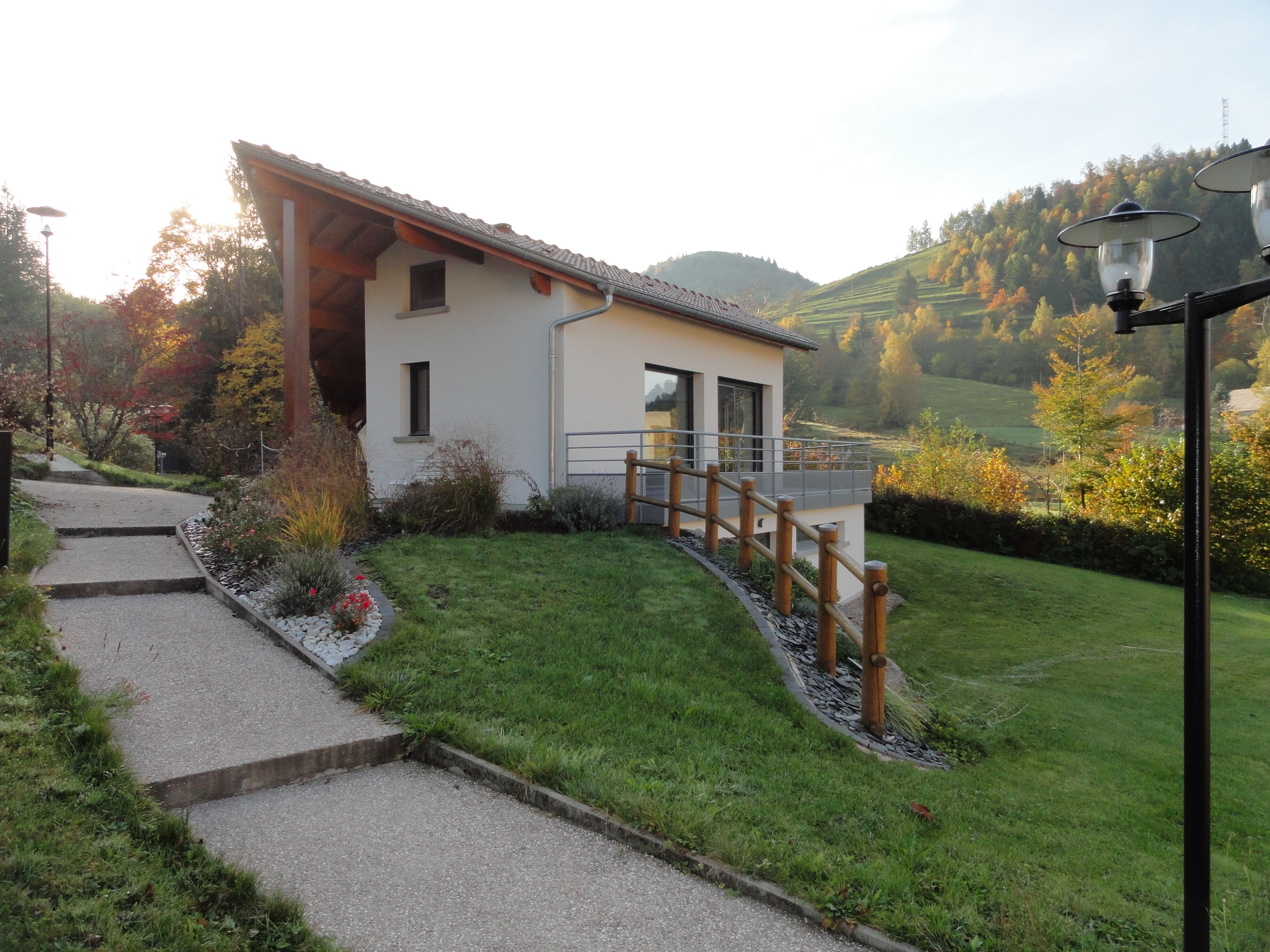 A modern house with a sloped roof, a wooden deck, and a paved pathway leading to the entrance.