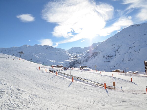 A snow-covered ski slope with ski lifts, buildings, and mountains in the background.