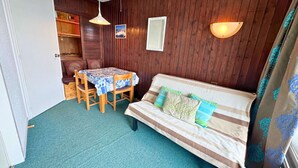 Une pièce chaleureuse avec un mur en bois, un canapé à rayures, une table avec des chaises et deux lampes fixées au mur.