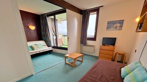 Une chambre à coucher avec un lit, un banc en bois, une télévision et une fenêtre avec des rideaux.