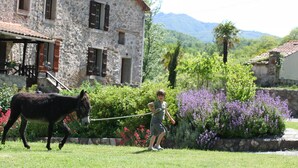 A stone building with a balcony and a child leading a donkey in a garden with flowers and trees. - Charming cottages 3 stars, 20m pool, WIFI, dream setting, river (Le Tech)