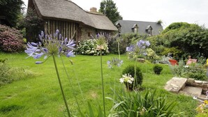 Ein traditionelles Haus mit einem Reetdach, umgeben von einem gepflegten Garten mit verschiedenen Pflanzen und Blumen.