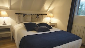 Ein Schlafzimmer mit einem Bett, zwei Nachttischen, zwei Lampen, einem Fenster mit Vorhängen und einer Heizung.