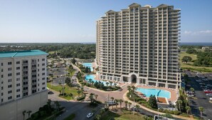 A high-rise hotel with multiple balconies, a swimming pool, and a parking area.