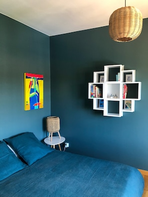 Um quarto com uma cama, uma estante na parede, um candeeiro suspenso e um quadro.