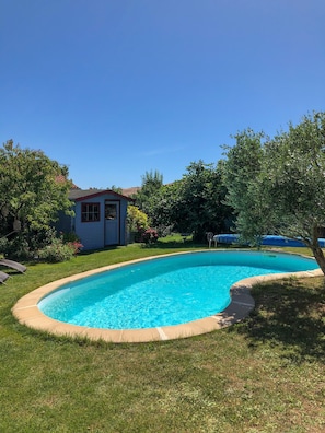 Piscina de borda curva, rodeada por grama e árvores.