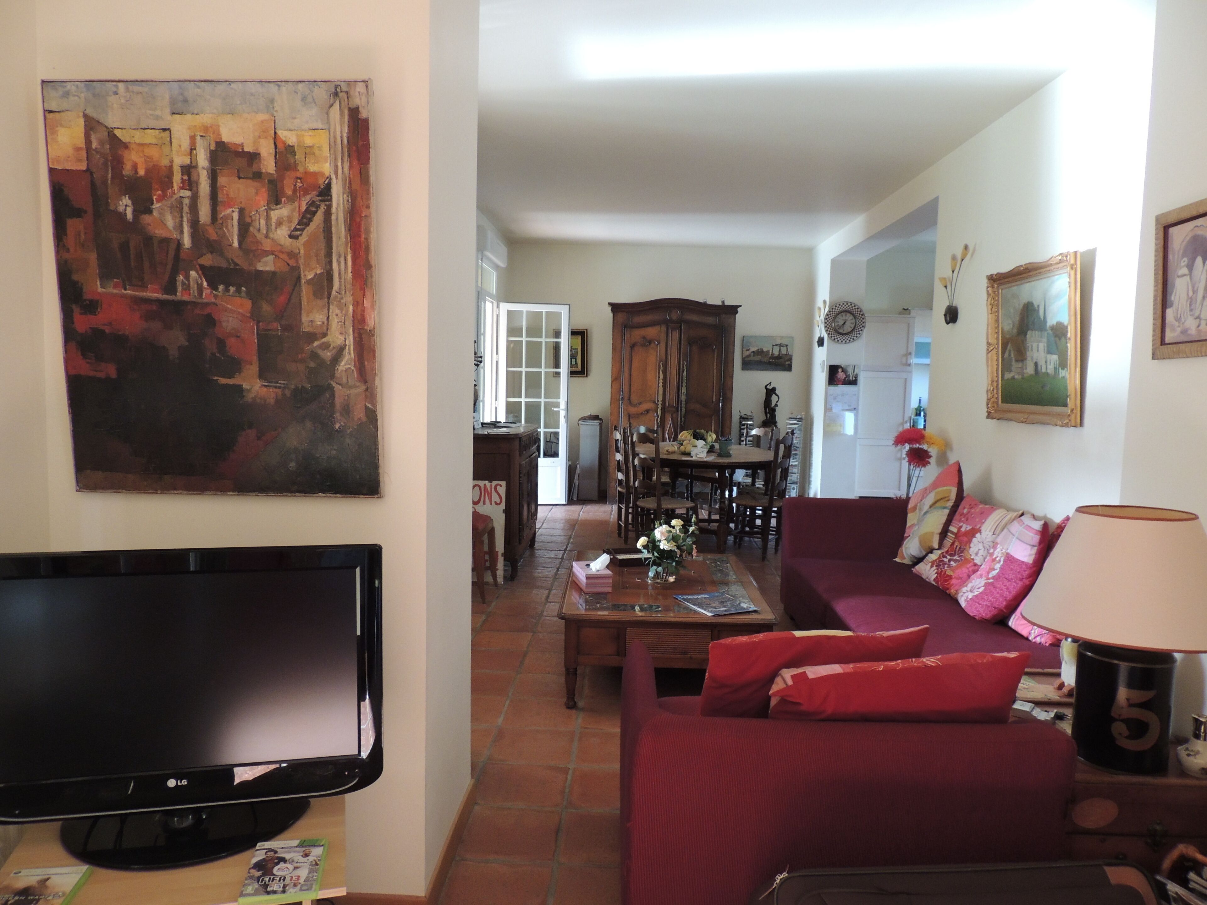 Una sala de estar con televisor de pantalla plana, un sofá rojo y una zona de comedor con mesa y sillas de madera.
