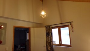 Une pièce avec un plafond en bois, une fenêtre ornée de rideaux à motifs et un luminaire suspendu.