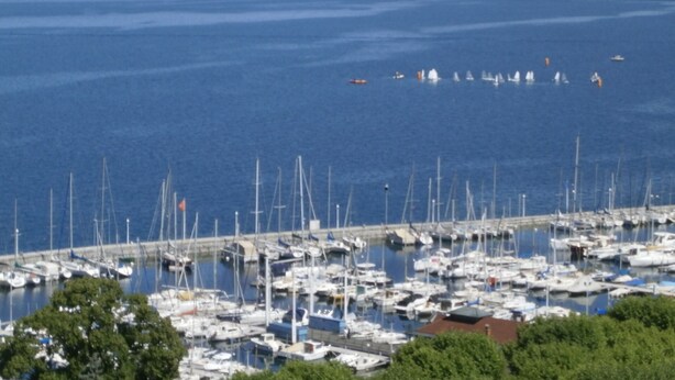 Un port de plaisance où de nombreux bateaux sont amarrés, une jetée qui s’avance dans l’eau et une côte lointaine.
