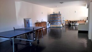Una habitación amplia con mesa de ping pong, lavadora y un barril grande.