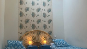Una habitación pequeña y acogedora con dos camas, un ventilador de pared y un tragaluz.