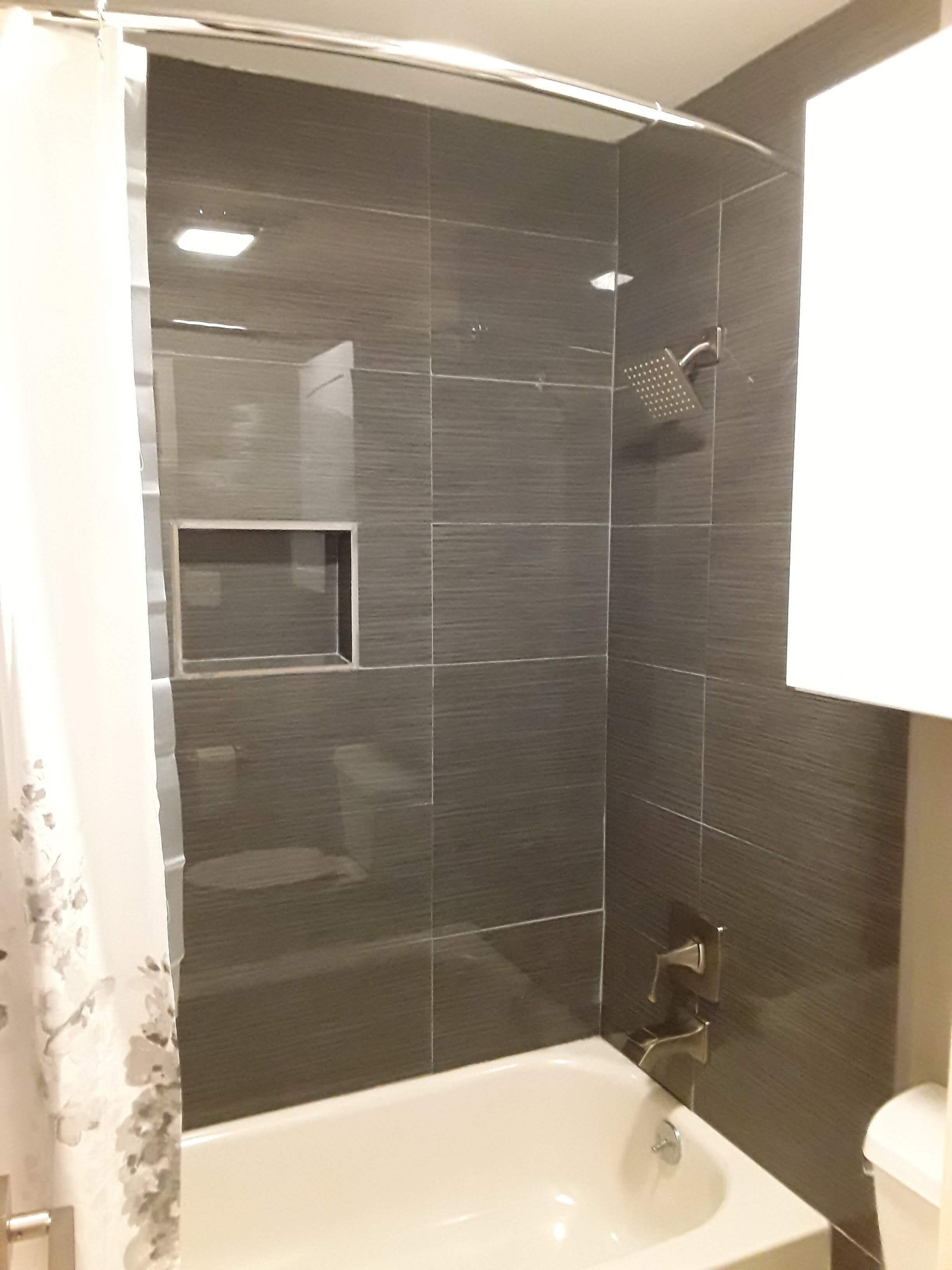 A modern bathroom with dark tiles, a white bathtub, and a shower.