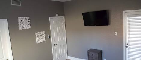 A room with a ceiling fan, a flat-screen TV mounted on the wall, and a small cabinet against the wall.