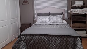 Una camera da letto con un letto, una finestra con persiane, uno scaffale con asciugamani piegati e una decorazione a parete con la scritta 'adventure'.