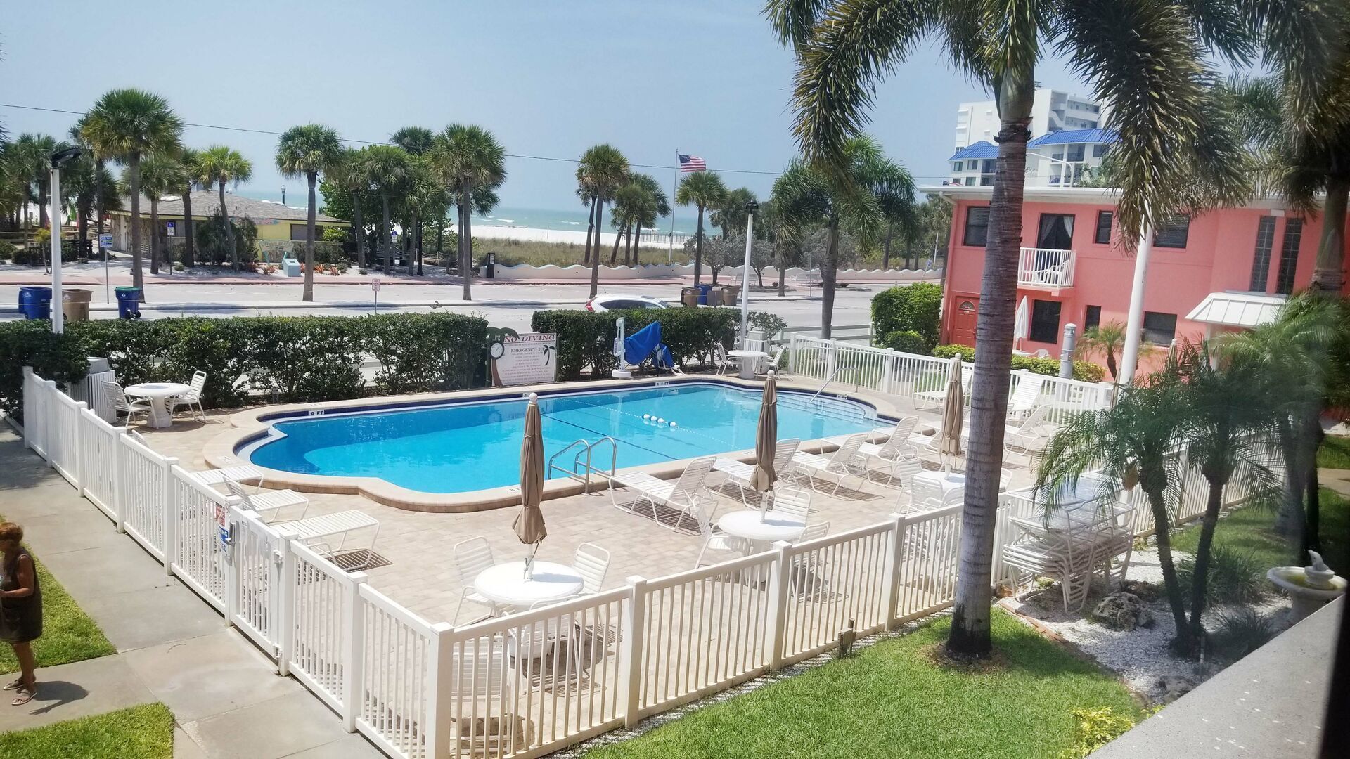 Piscina com deck cercado, cadeiras de descanso e vista para a praia e o oceano.