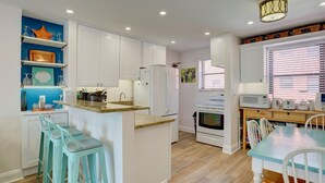 A modern kitchen with white cabinets, a granite countertop, a built-in oven, and a dining area with a table and chairs. - Newly Remodeled Poolside Condo with Gorgeous Ocean-Front View - Sleeps 8 (St Pete Beach)