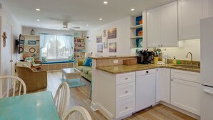 A compact kitchen with white cabinets, a dining area with a table and chairs, and a cozy seating area with a sofa and cushions. - Newly Remodeled Poolside Condo with Gorgeous Ocean-Front View - Sleeps 8 (St Pete Beach)