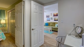 A room with a bed, a desk, and a chair. There is a door leading to another room. - Newly Remodeled Poolside Condo with Gorgeous Ocean-Front View - Sleeps 8 (St Pete Beach)