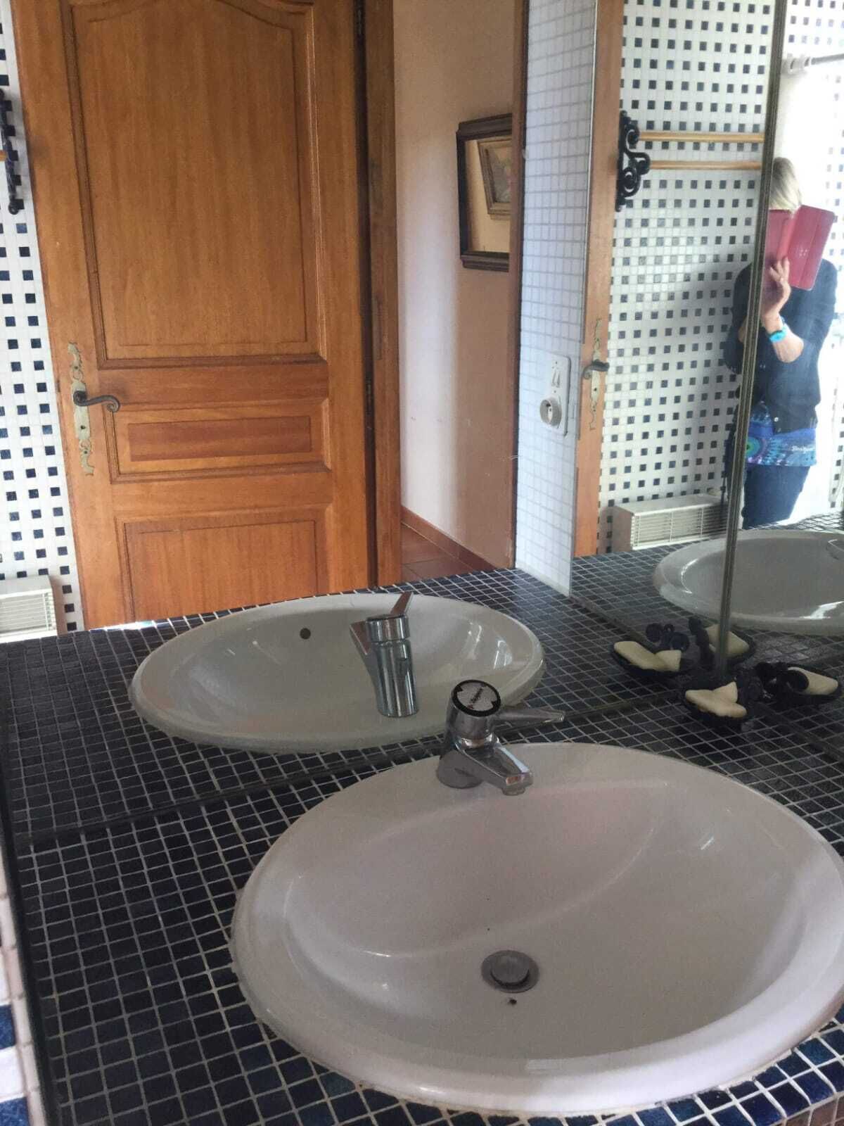 Een badkamer met twee wastafels, een houten deur en een betegelde spatwand.