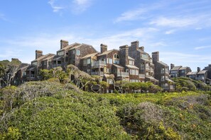 Situated on a lush hillside, this building features interconnected units with prominent chimneys and a variety of windows.