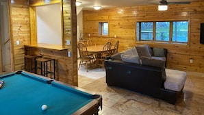 Una habitación acogedora con mesa de billar, paredes de madera, sofá y zona de comedor.