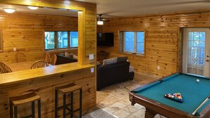 Interior de una cabaña de madera con mesa de billar, barra y zona de estar.