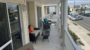 A covered porch with outdoor seating, a view of the street, and parked cars.