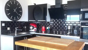A modern kitchen with a black and white color scheme, featuring a large black clock, a wooden island with stools, and black tiled backsplash. - PROMO FINISTERE SUD Villa sea view POOL /SPA indoor, heated (Plouhinec)