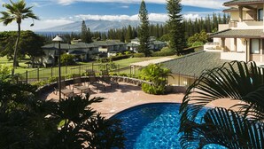 A resort with a swimming pool, lounge chairs, and a view of a mountain range.