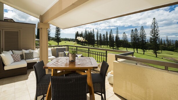 A balcony with a wooden table and chairs, a sofa, and a view of a golf course.