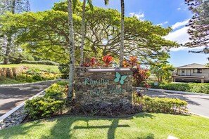 A stone sign with the text 'Kapalua Golf Villas' surrounded by lush greenery and trees.