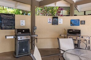 Un espace extérieur avec une piscine, un panneau indiquant les heures d’ouverture et le règlement de la piscine, un barbecue, une table avec une chaise et un panneau interdisant de fumer.